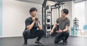 ダンベルスクワットを指導者と行う男性